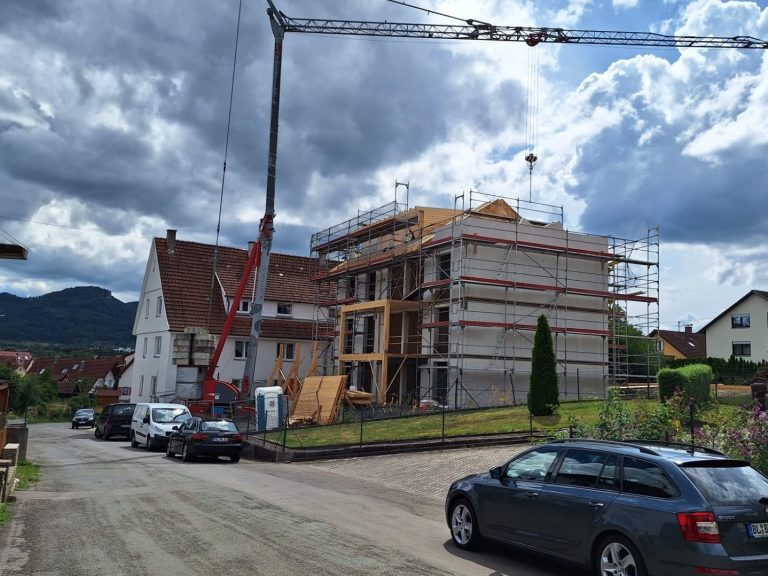 Bau eines mehrstöckigen Gebäudes mit Kran und Fahrzeugen auf der Straße.