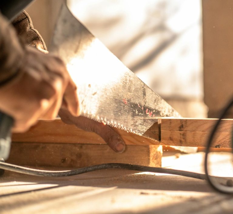 Ein Handwerker sägt ein Holzstück mit einer Handsäge in einem hellen Raum.