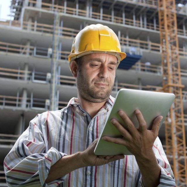 Bauleiter nutzt ein Tablet auf einer Baustelle mit einem Baugerüst im Hintergrund.