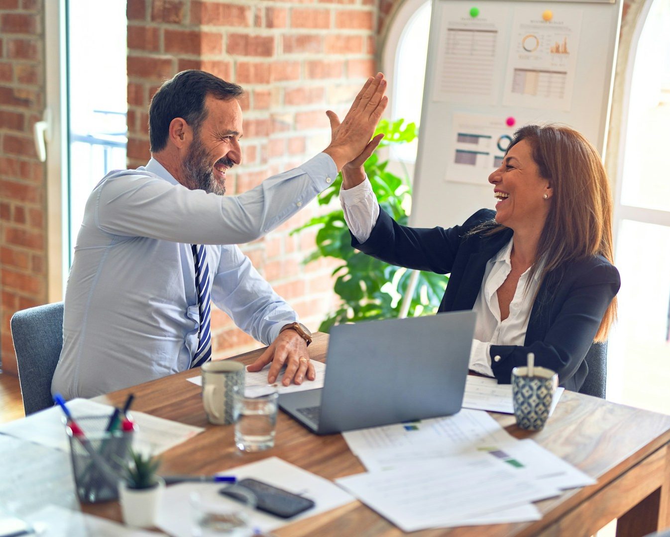 Zwei Personen lachen und geben sich am Tisch ein High-Five in einem modernen Büro.