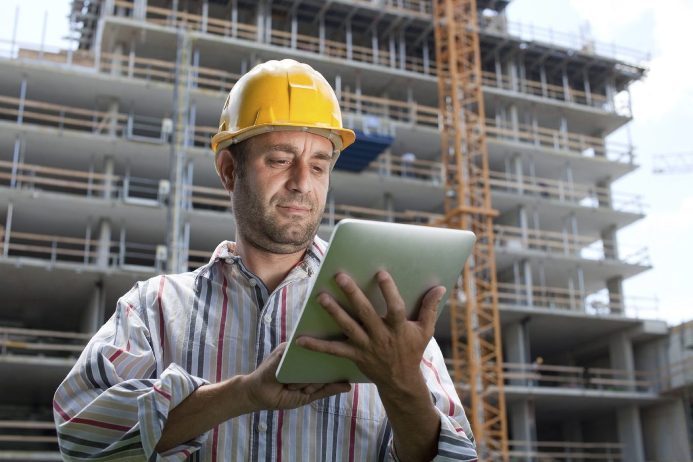 Mann mit Helm nutzt ein Tablet vor einem im Bau befindlichen Gebäude.